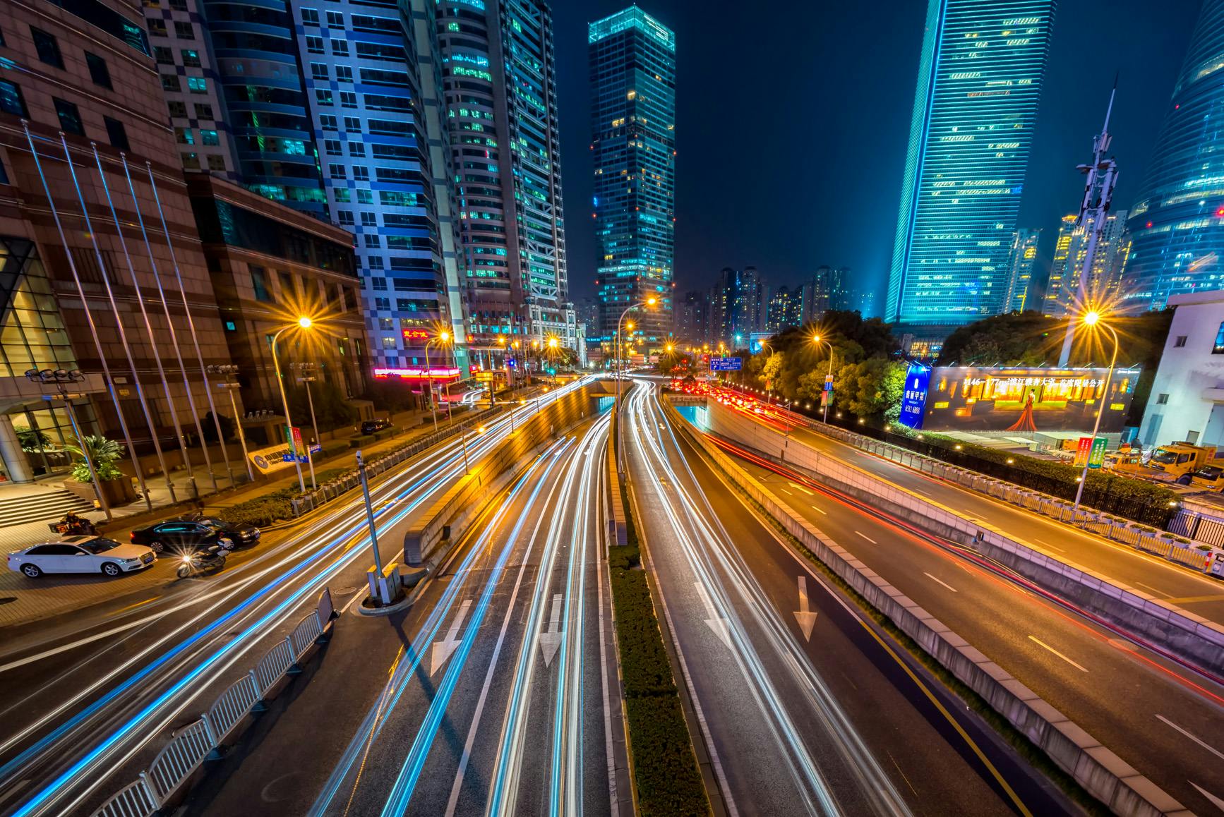 Dynamic long exposure night shot of urban cityscape with vibrant light trails and towering skyscrapers.